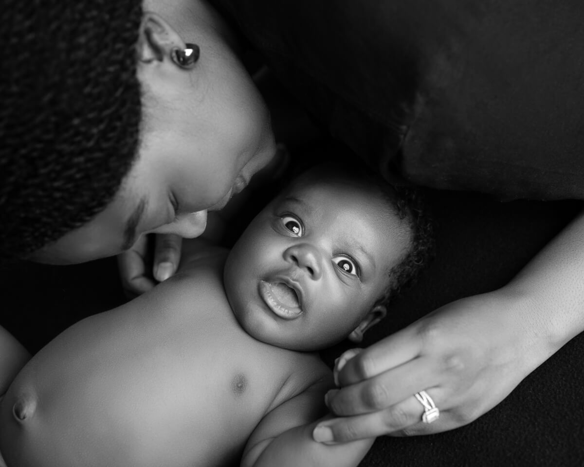 A woman leans over her newborn baby. The baby is looking directly into the camera. 