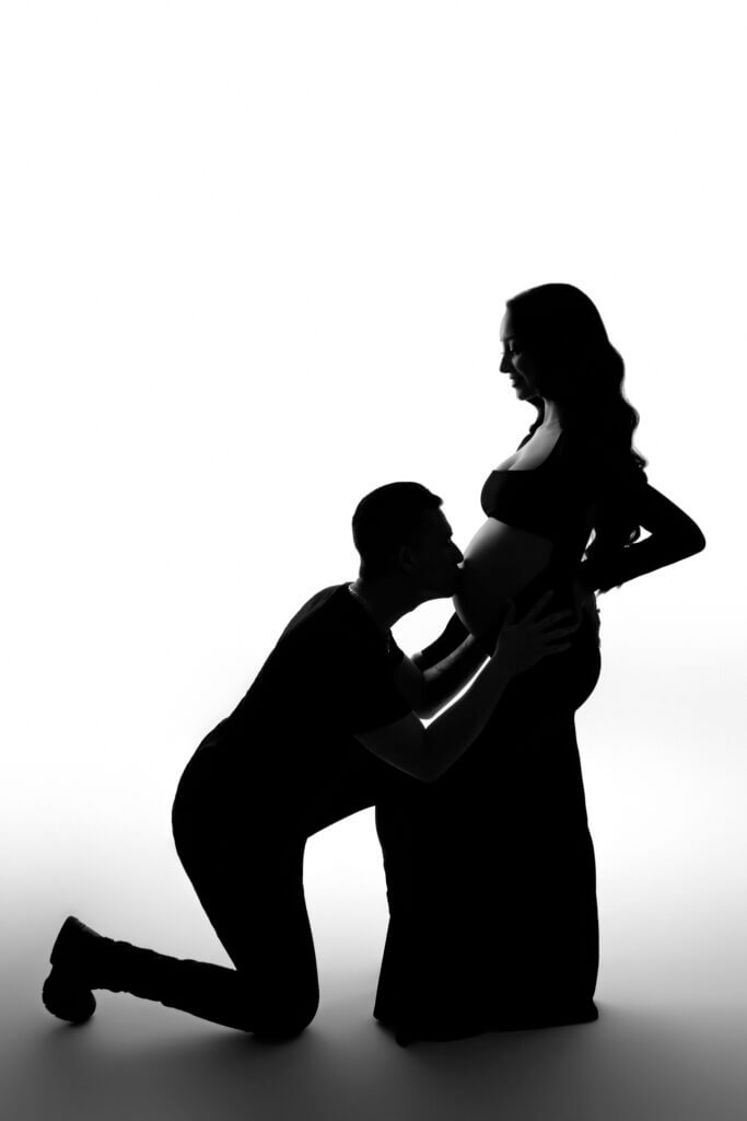 black and white silhouette of man kneeling to kiss wife's pregnant belly