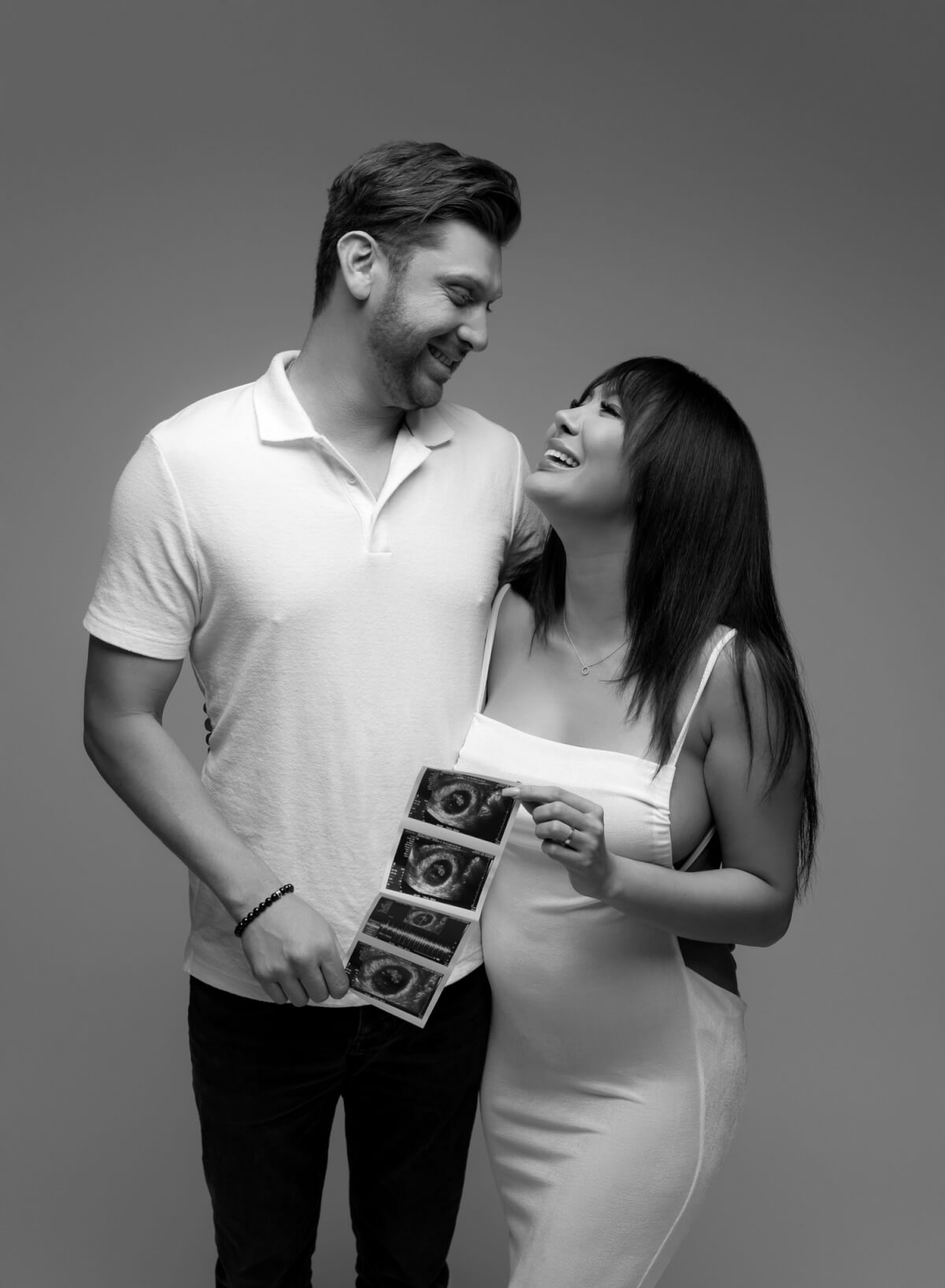 A couple stands next to one another. They are holding an ultrasound photo.
