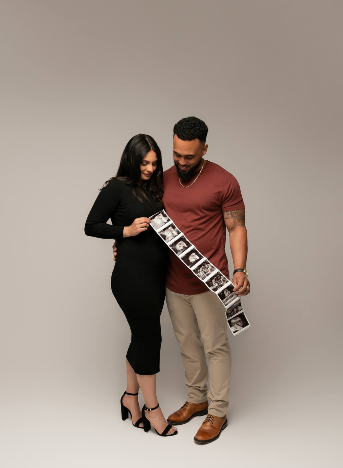 A full color photo featuring a man and a woman standing next to each other. They are holding a string of ultrasound photos.