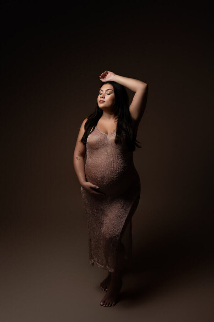 woman wearing gold knit dress holding pregnant belly moody lighting