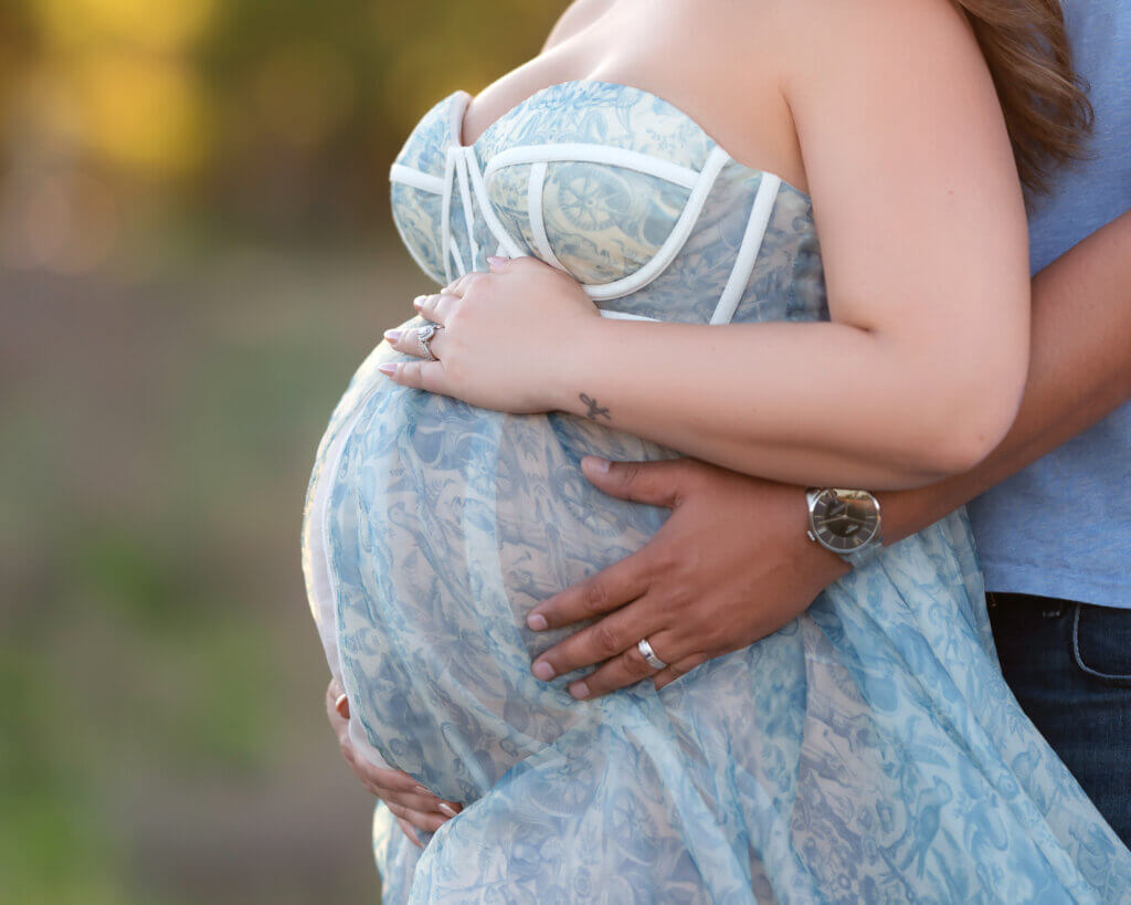 pregnant woman blue floral dress with her and husbands hands on belly