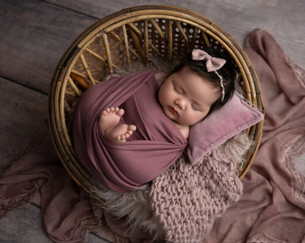 baby girl wrapped in raspberry wrap in rattan basket for newborn photoshoot in austin