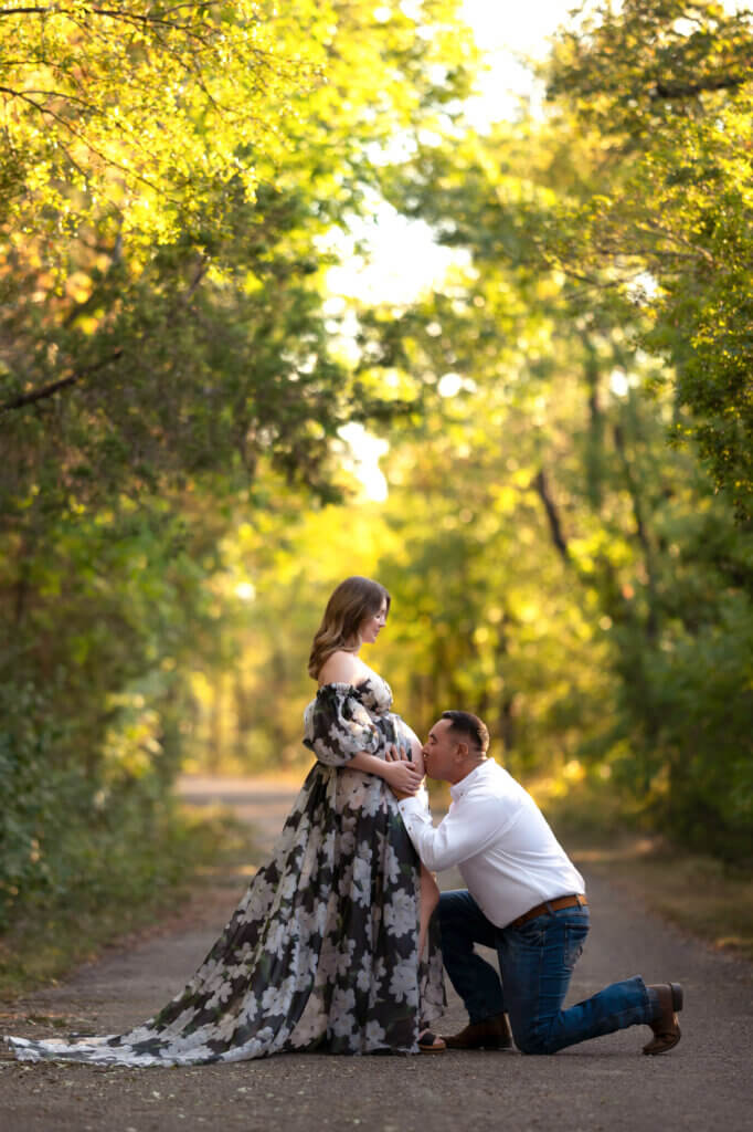 pregnant couple during outdoor photshoot with floral dress and man kissing her belly
