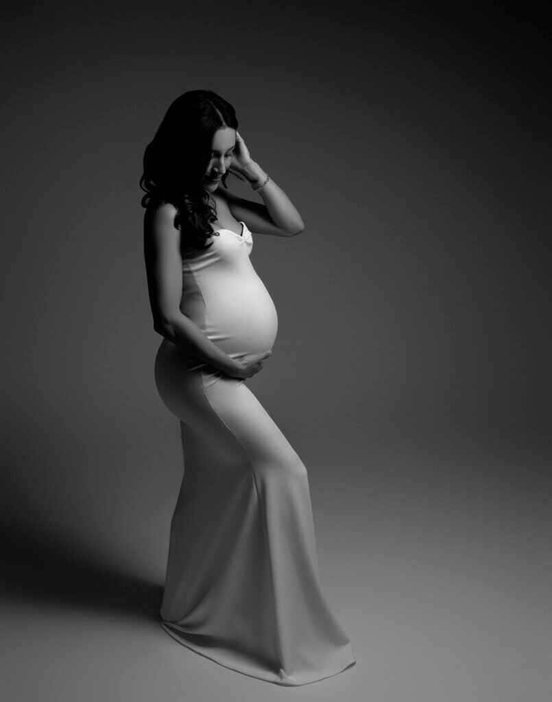 black and white woman wearing white fitted maternity gown touching her belly