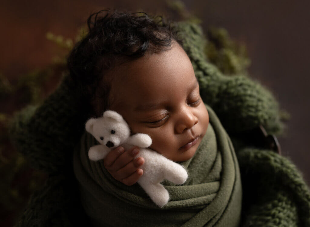 sleeping baby wrapped in green holding white bear