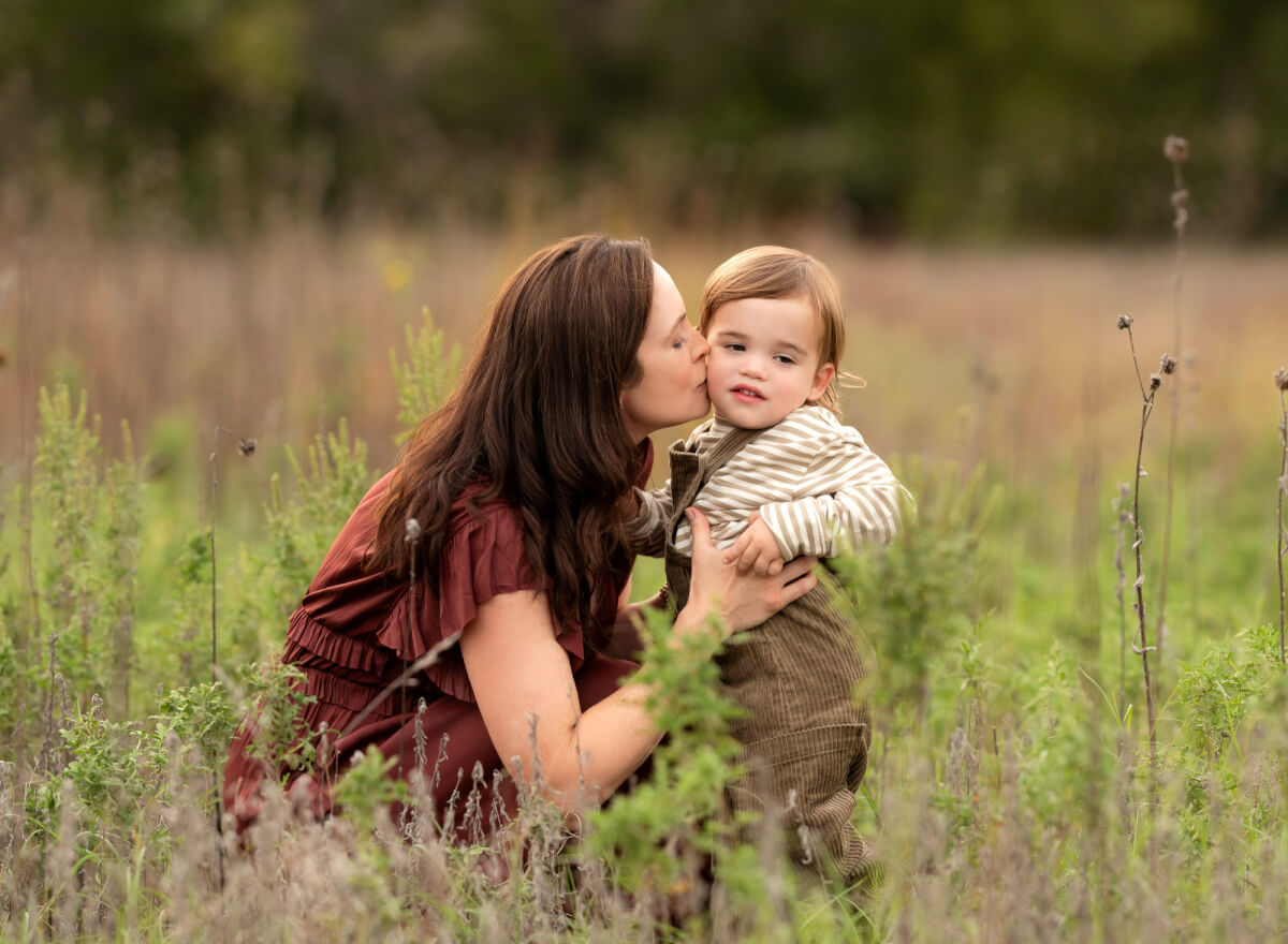 mom kissing toddler sun in tall grass