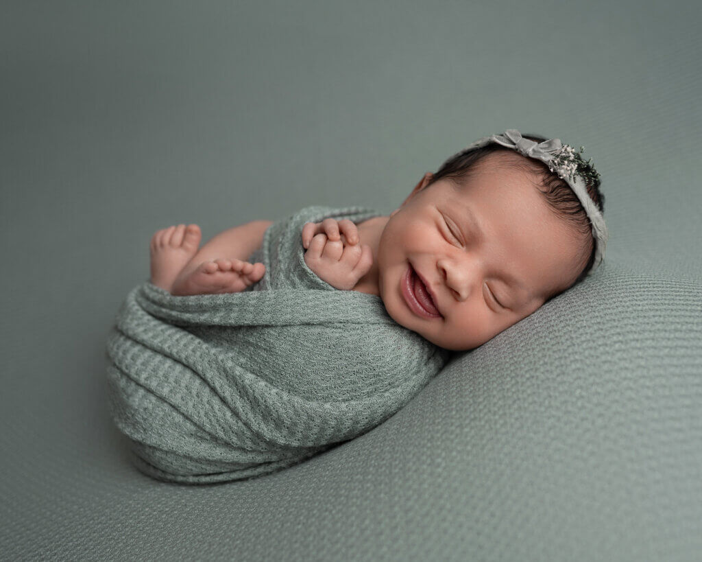 smiling baby swaddled in sage green textured wrap