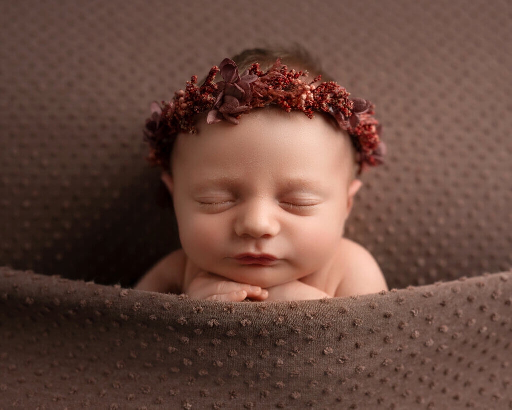 baby girl with pink floral crown tucked into a mauve polka dotted bed