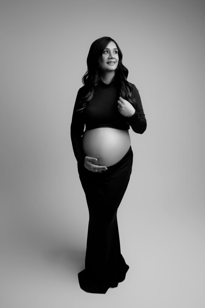 Expectant mother in black cradling her bare belly and smiling, photographed in a Leander maternity studio.