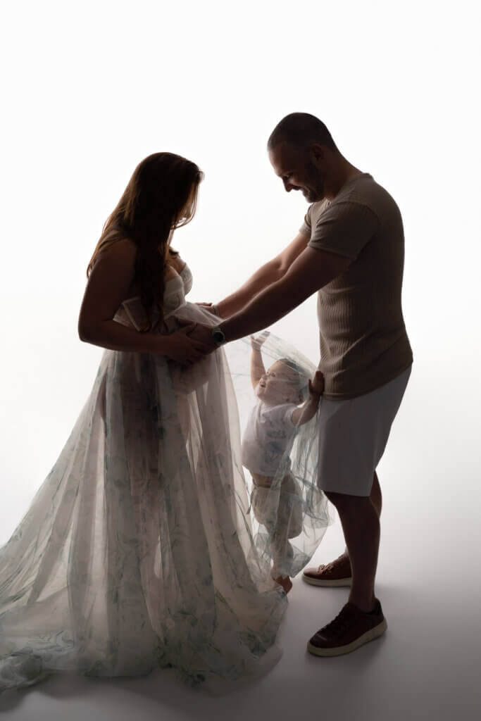 Expecting couple and their toddler backlit in a flowing gown during a maternity photoshoot in Leander, Texas