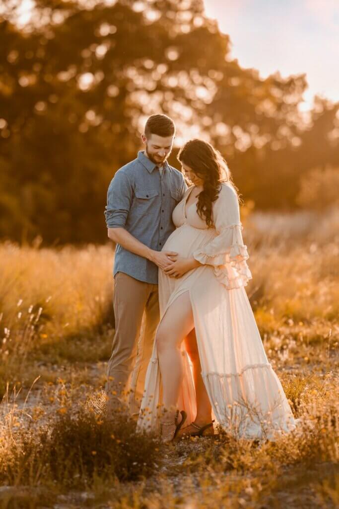 Couple with hands on the baby bump in a sunlit field for babymoon photography in Austin, Texas