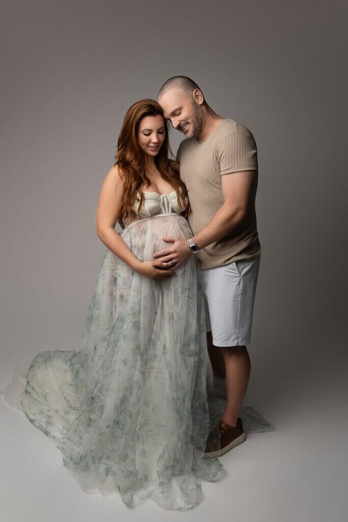 Couple in a studio maternity portrait with mom in a floral gown for a babymoon photo session