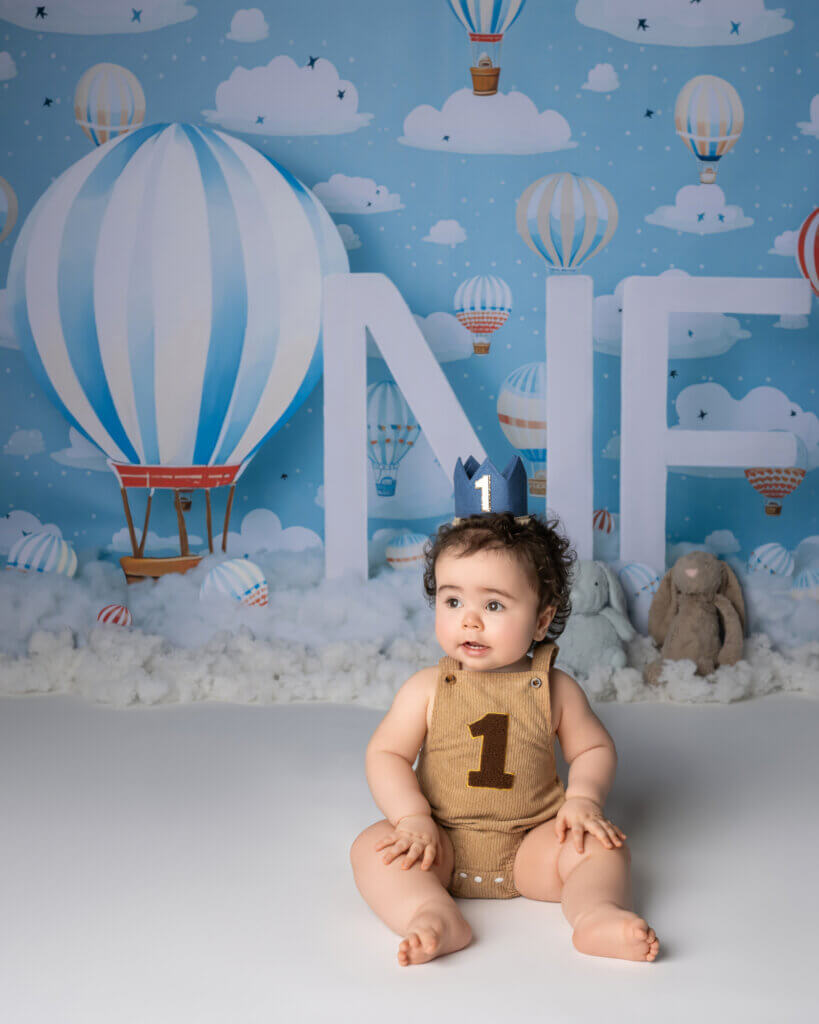 One year old boy in a party hat on a hot air balloon set at a first birthday photoshoot in Austin