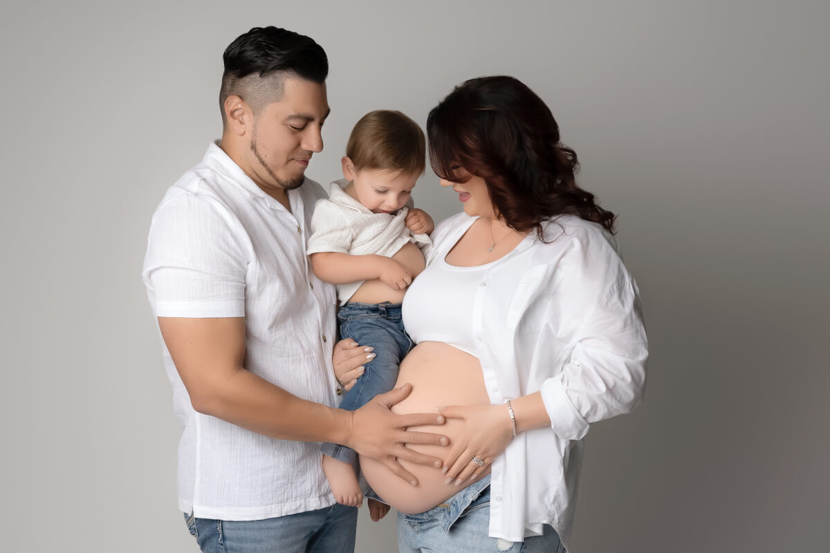Family in white shirts and jeans holding their toddler during a maternity session with an Austin, Texas maternity photographer