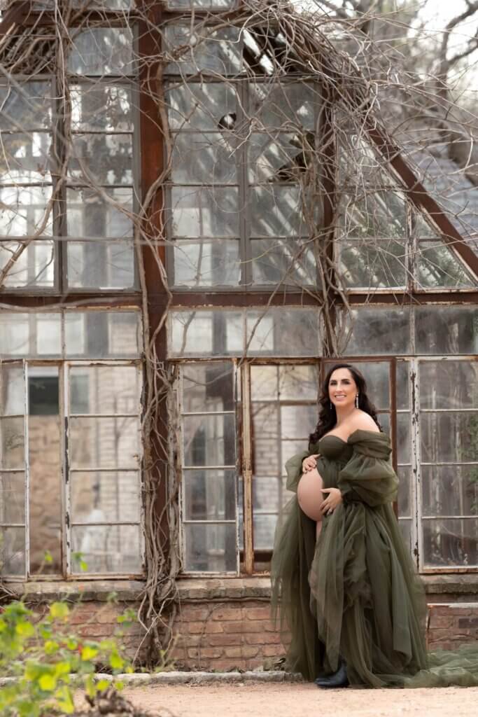 Pregnant woman in a green gown inside a vintage greenhouse at an Austin maternity photo location