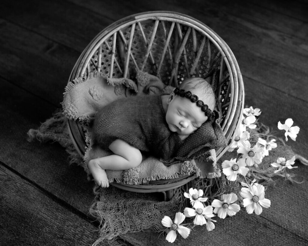 Newborn posed in a woven basket with white flowers by a professional newborn photographer in Austin