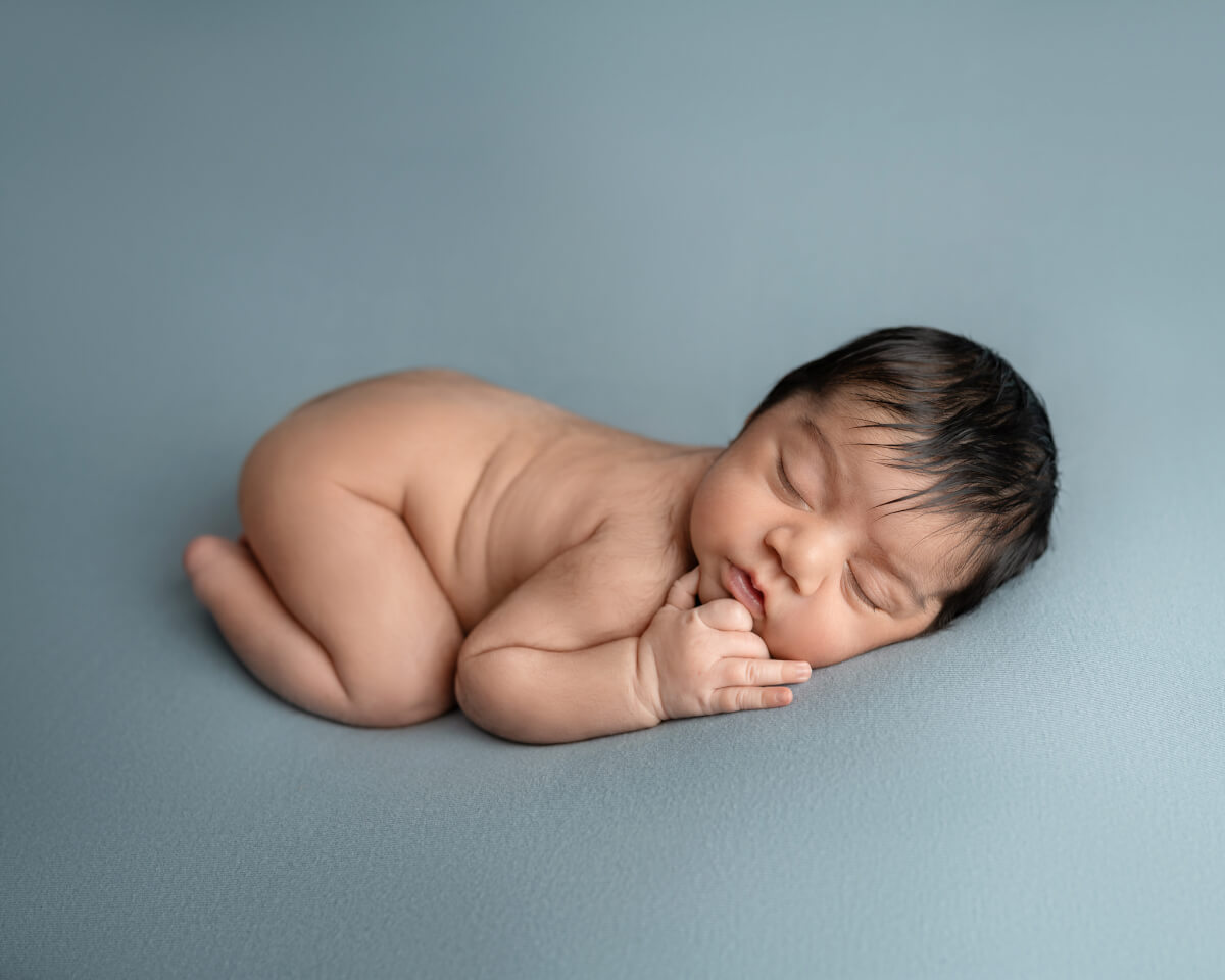 Newborn boy sleeping on a dusty blue backdrop in a Leander, Texas newborn photography studio