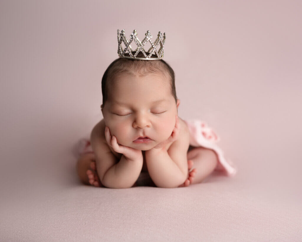 Newborn with a tiny crown posed on a neutral backdrop during a professional newborn session near Austin